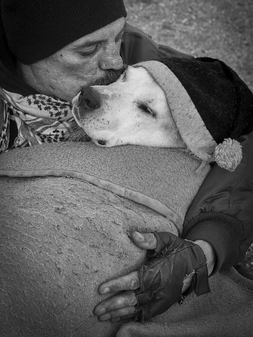 <p>A man gives a kiss to his hat-wearing dog as they cuddle together under a blanket. (Polina Ulyanova/PA Wire)</p>
