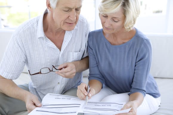 Senior couple looking at paperwork with concerned expressions.