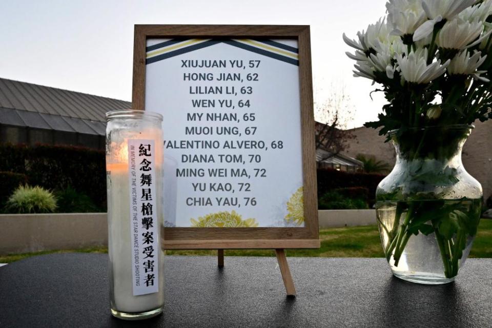 A frame bears the names and ages of 11 people killed in the Monterey Park shooting. A lit votive candle and vase of white flowers sit next to the frame.