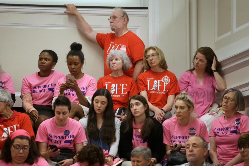 Proponents of a proposed Massachusetts legislative bill, called the "Roe Act" by supporters, wear pink shirts, while opponents of the bill wear red shirts as they listen during a public hearing at the Statehouse in Boston on June 17, 2019.
