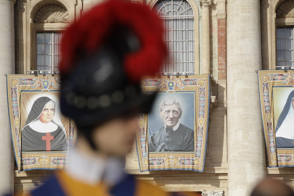 A Swiss guard stands guard as the tapestries of Cardinal John Henry Newman, right, and Giuseppina Vannini are seen in background, in St. Peter's Square at the Vatican, Sunday, Oct. 13, 2019. Pope Francis canonizes Cardinal John Henry Newman, the 19th century Anglican convert who became an immensely influential thinker in both Anglican and Catholic churches, and four other women. (AP Photo/Alessandra Tarantino)