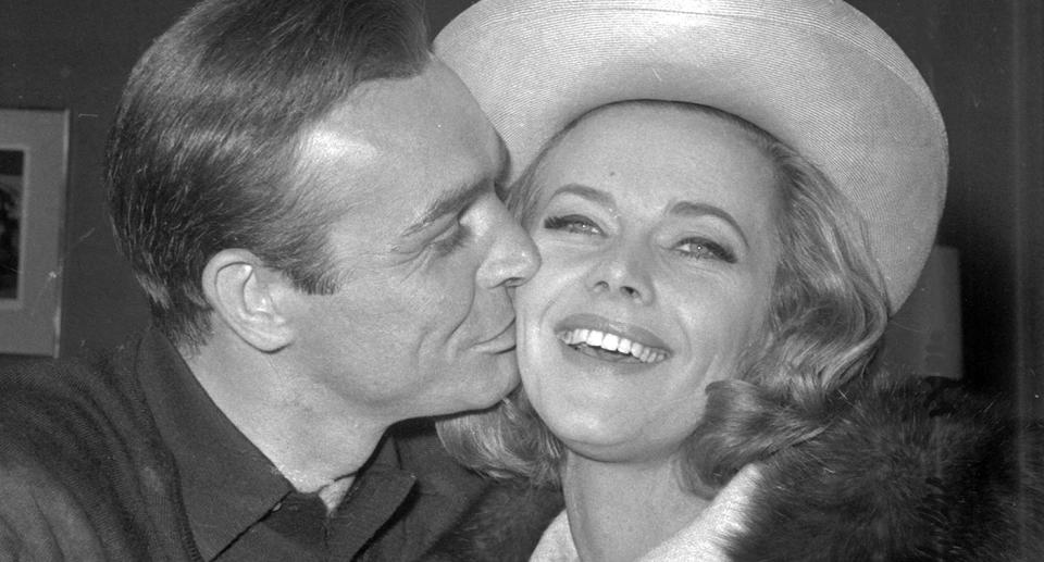 FILE - In this B/W file photo dated March 25, 1964, British actor Sean Connery kisses actress Honor Blackman during a party at Pinewood Film Studios, in Iver Heath, England.  Blackman, the actor best-known for playing Bond girl Pussy Galore, hasdied of natural causes unrelated to coronavirus, aged 94, according to an announcement Monday April 6, 2020. (AP Photo, FILE)