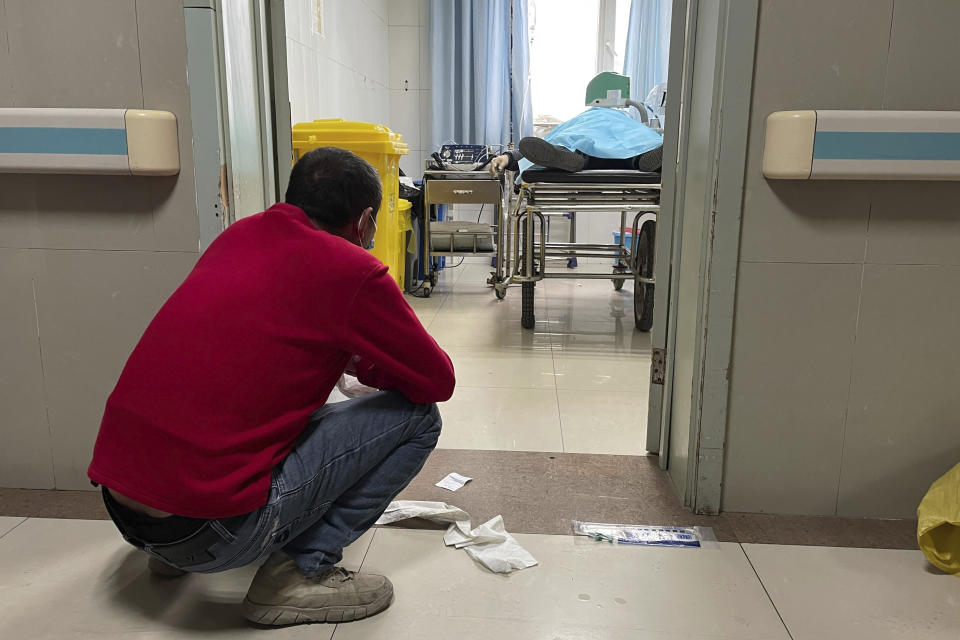 FILE - A man squats outside a treatment room as an elderly person receives help with breathing via a manual ventilator pump at the emergency department of the Baoding No. 2 Central Hospital in Zhuozhou city in northern China's Hebei province, Dec. 21, 2022. China's sudden reopening after two years holding to a "zero-COVID" strategy left older people vulnerable and hospitals and pharmacies unprepared during the season when the virus spreads most easily, leading to many avoidable deaths, The Associated Press has found. (AP Photo, File)