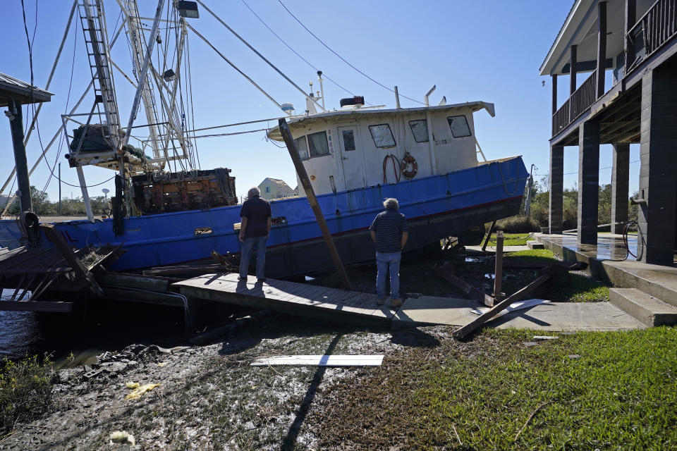 Boat owner Ricky Mitchell, left, and his friend Buck, no last name given, surveys damage to his boat that washed up against the home of Ray Garcia, in Lakeshore, Miss., Thursday, Oct. 29, 2020. Hurricane Zeta passed through Wednesday with a tidal surge that caused the boat to become unmoored. (AP Photo/Gerald Herbert)