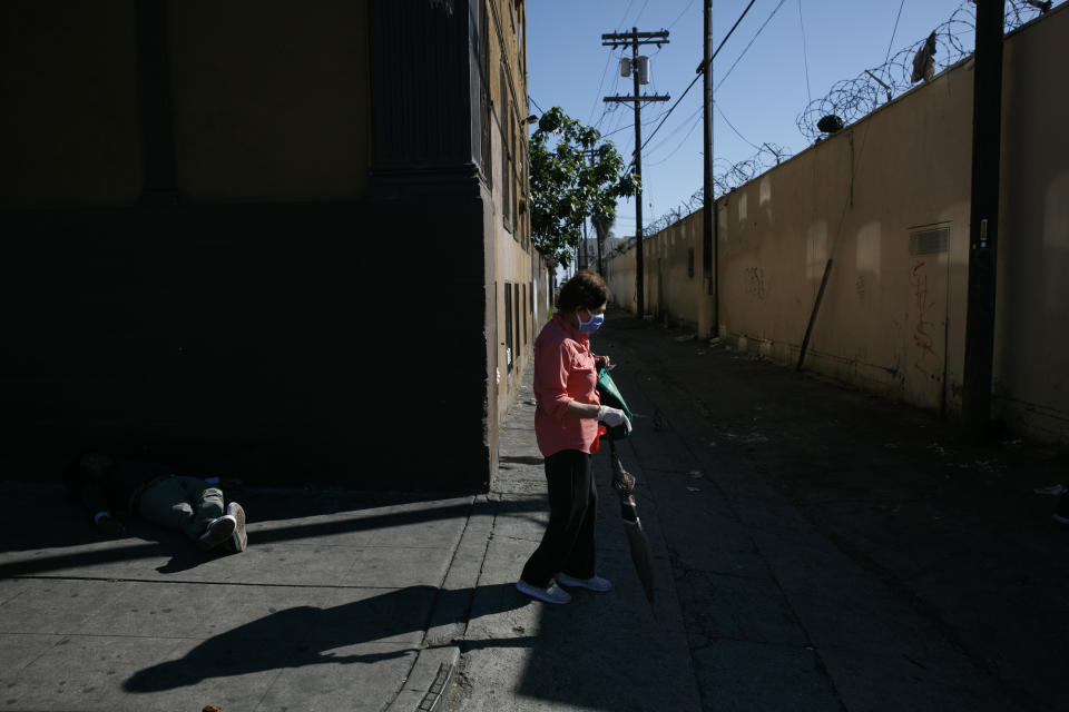 A woman with a mask and protective gloves walks past a homeless man napping on the street amid the coronavirus pandemic in the Westlake neighborhood of Los Angeles, Thursday, May 21, 2020. While most of California is welcoming a slight return toward normal this holiday weekend, Los Angeles will not be joining the party. The nation's largest county is not planning to reopen more widely until the next summer holiday, July 4th, because of a disproportionately large share of the state's coronavirus cases and deaths that have hampered the county's ability to rebound and meet strict criteria to get more people back to work.(AP Photo/Jae C. Hong)