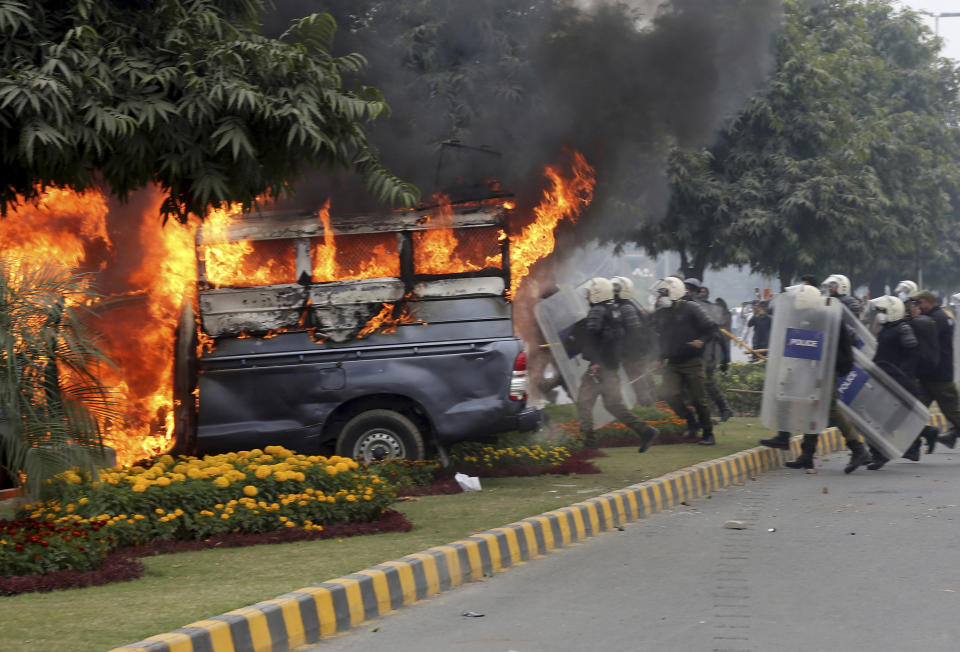 Police officers gather next to a burning police vehicles set on fire by angry lawyers during clashes in Lahore, Pakistan, Wednesday, Dec. 11, 2019. Hundreds of Pakistani lawyers, angered over alleged misbehavior of some doctors toward one of their colleagues last month, stormed a cardiology hospital in the eastern city of Lahore, setting off scuffles with the facility's staff and guards that left heart patients unattended for several hours. (AP Photo/K.M. Chaudary)