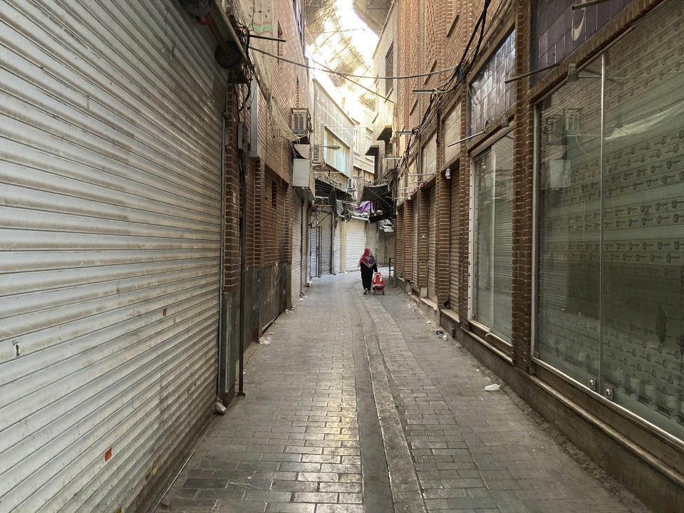 A woman carries her cart past closed shops of Tehran's Grand Bazaar, Iran, Tuesday, Nov. 15, 2022. Many shops at Grand Bazaar in Iran's capital city were closed Tuesday amid strike calls following the September death of a woman who was arrested by the country's morality police. (AP Photo/Vahid Salemi)