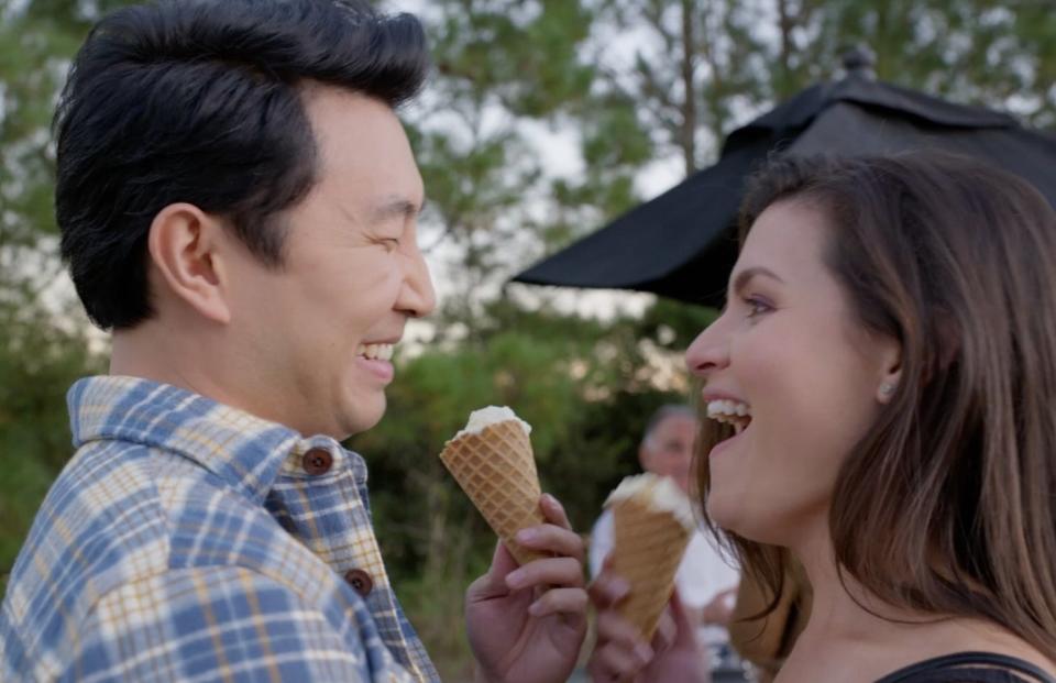 A man and a woman share ice cream cones, laughing.