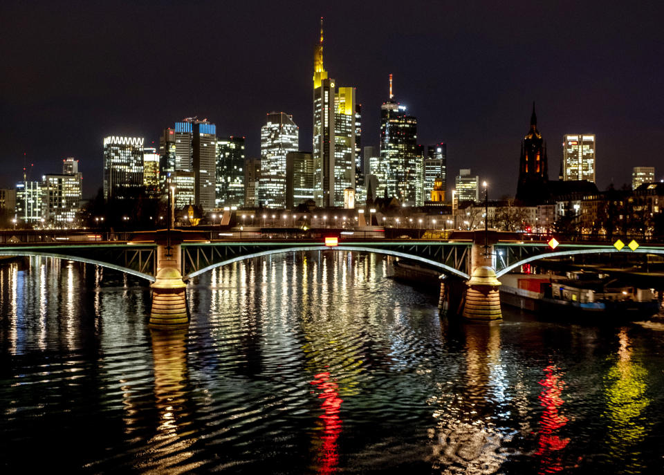 The lights of a bridge are reflected in the river Main in Frankfurt, Germany, Thursday, Jan. 21, 2021. In background are the buildings of the banking district. (AP Photo/Michael Probst)