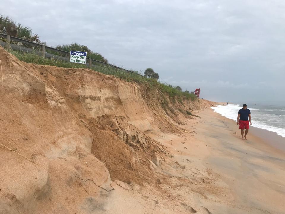 A man walks by a drop-off on Friday where there had previously been a sand ramp to reach the beach near State Road 100 and Ocean Shore Boulevard north of the pier in Flagler Beach. Recent erosion has left behind the "cliffs" and eroded other parts of the beach.