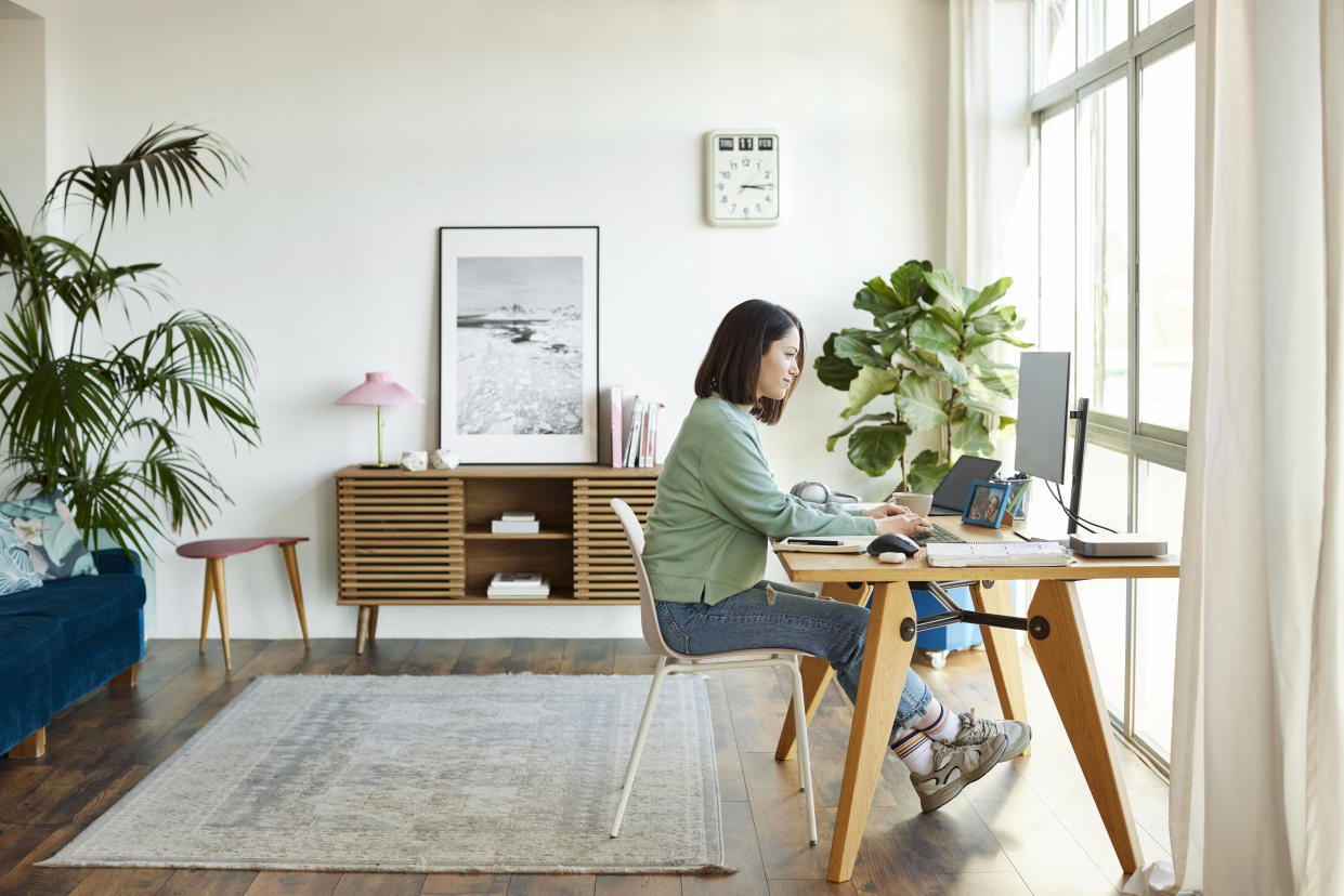 Side view of busy female entrepreneur using computer at home office. Businesswoman is working while sitting on chair at table. She is wearing casuals.