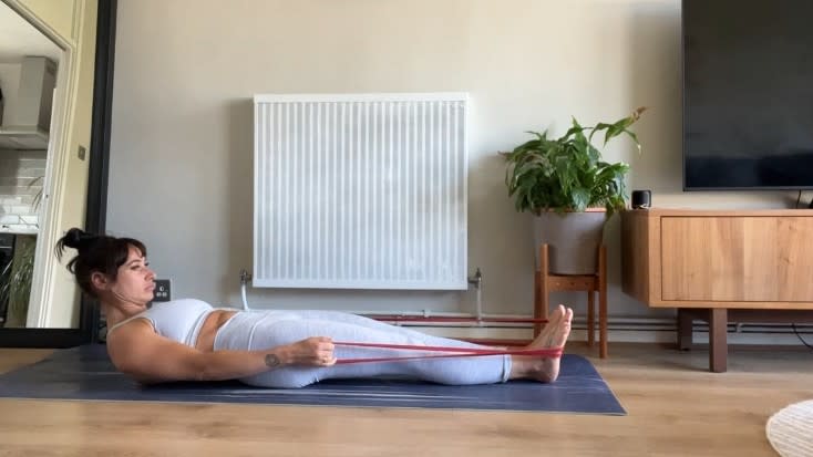 Writer Sam beginning roll up exercise while holding band wrapped around feet on exercise mat during home workout