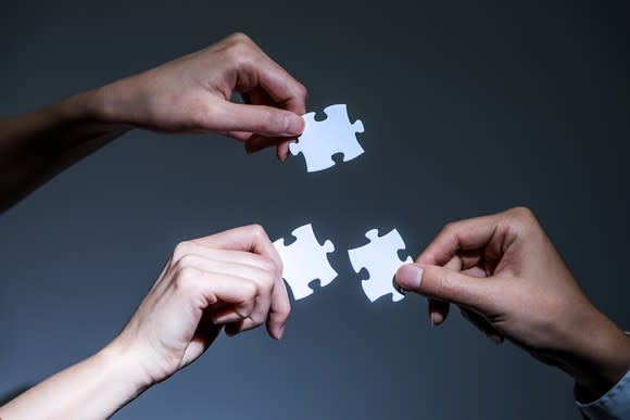 Three hands holding jigsaw puzzle pieces