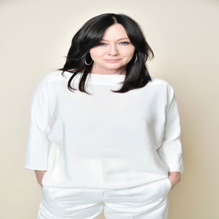 Shannen Doherty smiling with her hands in her pockets