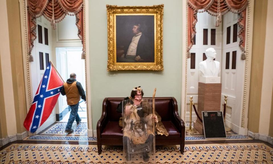 A pro-Trump rioter sits with a police shield outside the Senate chambers after breaching Capitol security.