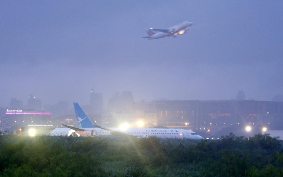 A Philippine Airlines passenger plane takes off while a Boeing passenger plane from China, a Xiamen Air, lies on the grassy portion of the runway of the Ninoy Aquino International Airport after it skidded off the runway while landing Friday, Aug. 17, 2018 in suburban Pasay city southeast of Manila, Philippines. All the passengers and crew of Xiamen Air flight MF8667 were safe and were taken to an airport terminal, where they were given blankets and food before being taken to a hotel. (AP Photo/Bullit Marquez)