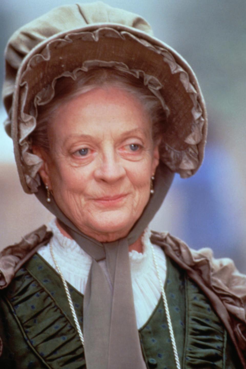 Maggie Smith wears a bonnet and period costume, portraying a character in historical attire