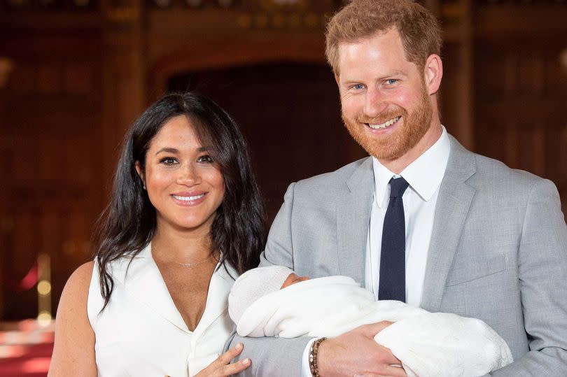 Prince Harry, Duke of Sussex (R), and his wife Meghan, Duchess of Sussex, pose for a photo with their newborn baby son, Archie Harrison Mountbatten-Windsor, in St George's Hall at Windsor Castle