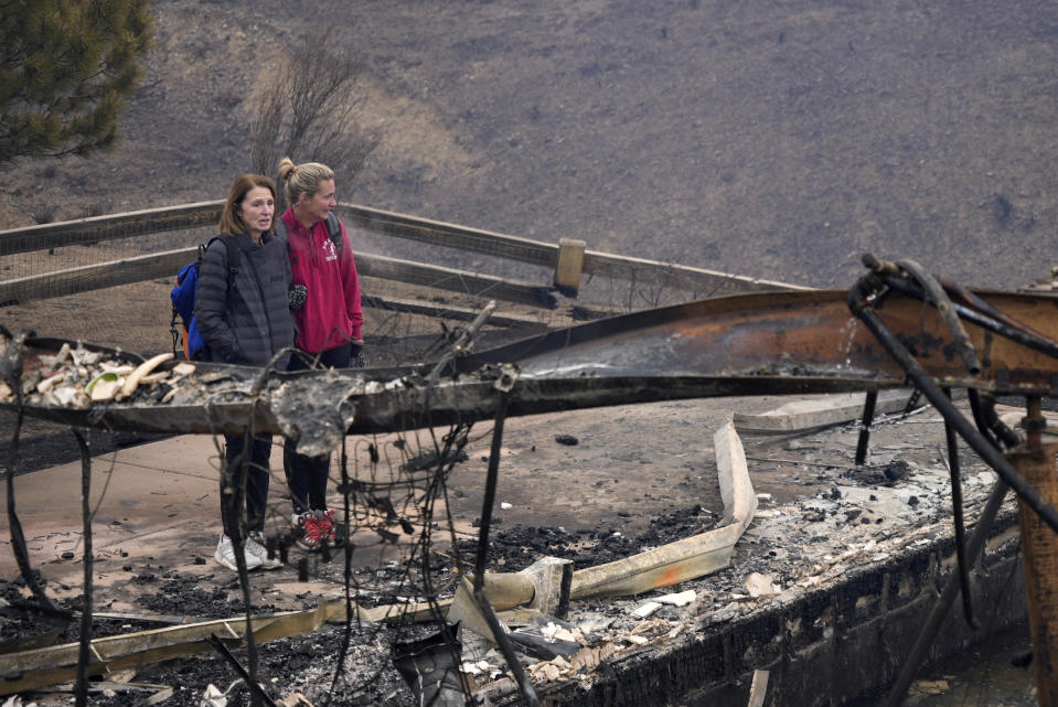 Cathy Glaab, left, surveys what's left of her home, accompanied by her daughter, Laura, in Superior, Colo on Friday, Dec. 31, 2021. Tens of thousands of Coloradans driven from their neighborhoods by a wind-whipped wildfire anxiously waited to learn what was left standing of their lives Friday as authorities reported more than 500 homes were feared destroyed. (AP Photo/Brittany Peterson)