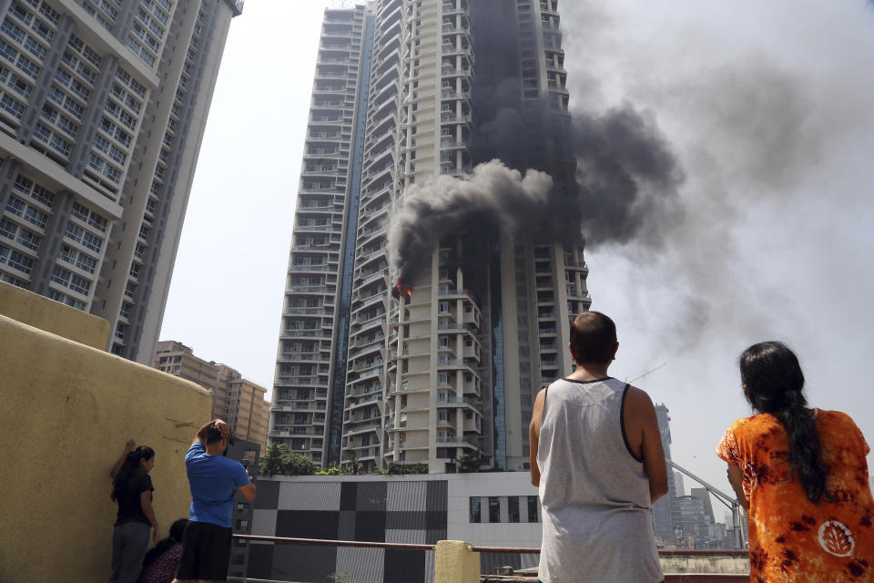 People watch a fire in a 61-story luxury apartment building in Mumbai, India, Friday, Oct. 22, 2021. Television images showed heavy black smoke billowing into the sky from the 19th floor apartment on Curry Road in south Mumbai, India's financial and entertainment capital. Fires are common in India, where building laws and safety norms are often flouted by builders and residents. (AP Photo)