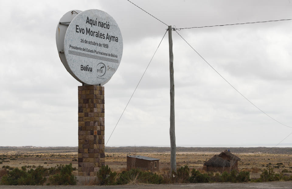 This Sept. 13, 2019 photo shows a towering stone post topped with a round billboard pointing out the straw roof home where Bolivia's President Evo Morales was born, on the outskirts of Orinoca, Bolivia. The two-room adobe house still has a thatched roof. It’s locked under bolt and its windows are boarded over. It’s the home where Morales was born and lived until age 15. (AP Photo/Juan Karita)