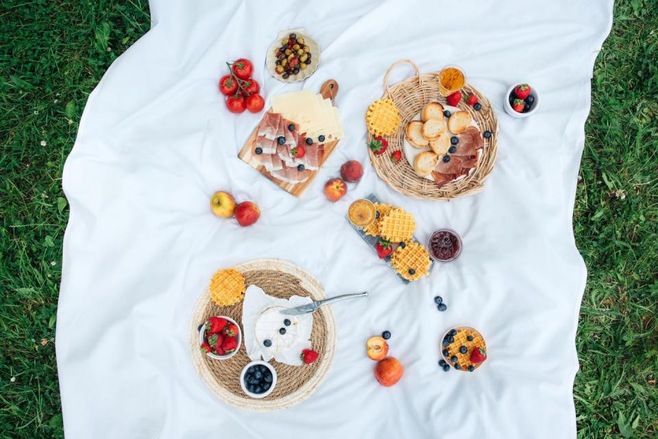 picnic with tasty and healthy food in nature nicely served picnic food in nature fruits, vegetables, cheese, jamon and croutons for a picnic spending time outdoors a white tablecloth or bedspread on the grass top view of a picnic