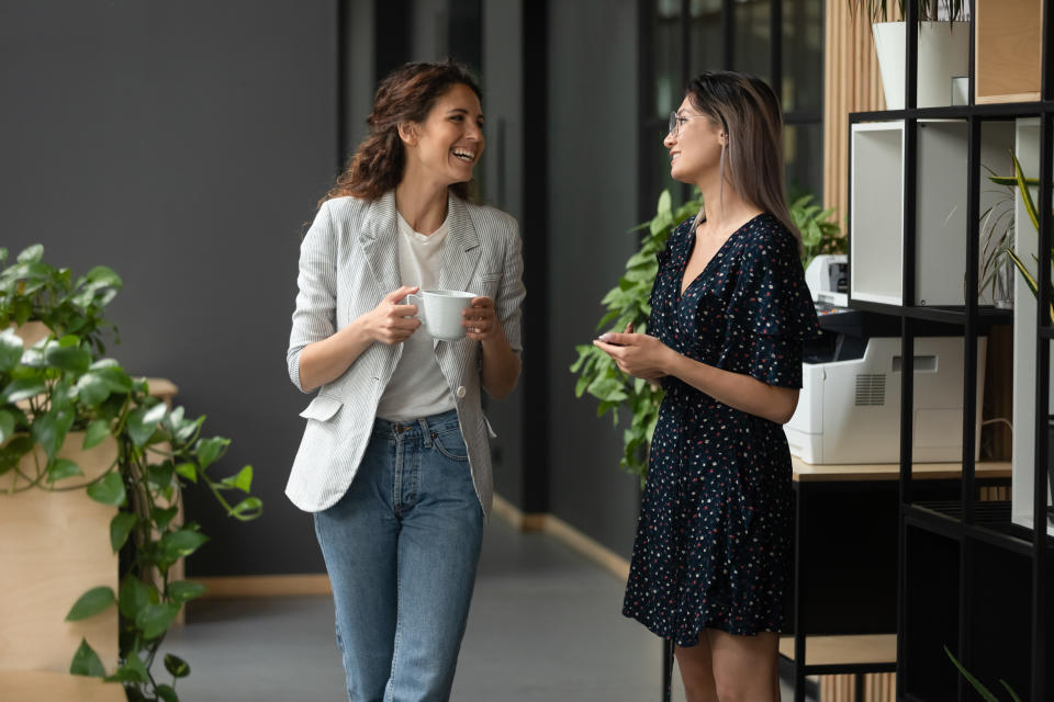 Asian and Caucasian ethnicity women colleagues met in office hall chatting enjoy friendly warm conversation, multi-ethnic mates having informal talk drink tea or coffee take break distracted from work