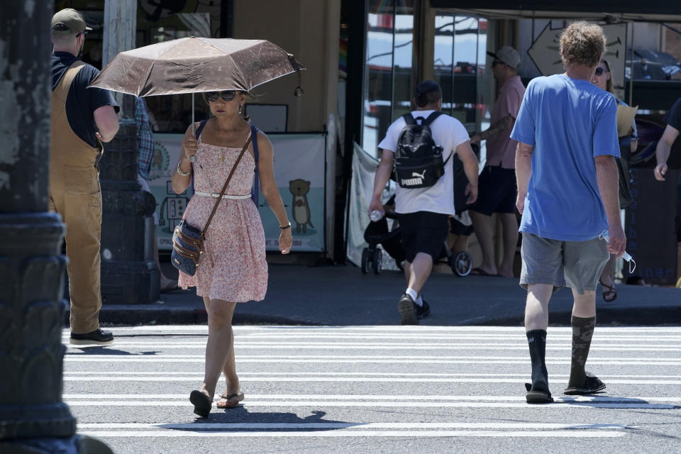 A person uses an umbrella for shade from the sun while walking near Pike Place Market, Tuesday, June 29, 2021, in Seattle. The unprecedented Northwest U.S. heat wave that slammed Seattle and Portland, Oregon, moved inland Tuesday — prompting an electrical utility in Spokane, Washington, to resume rolling blackouts amid heavy power demand. (AP Photo/Ted S. Warren)