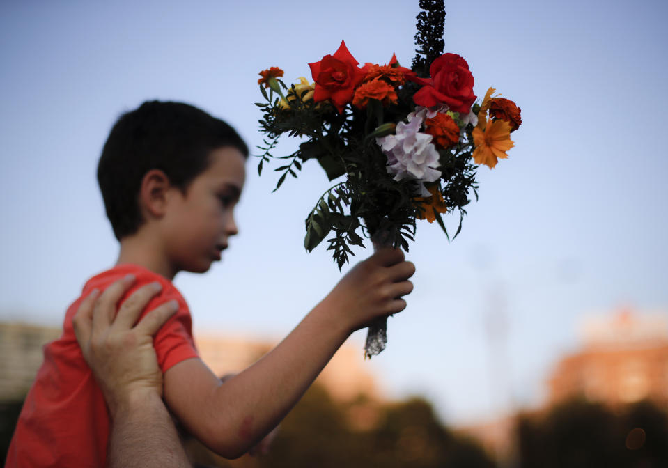 A child holds flowers outside the government headquarters in memory of a 15 year-old girl, raped and killed in southern Romania, after police took 19 hours from the moment she called the country's emergency hotline to intervene, in Bucharest, Romania, Saturday, July 27, 2019. Thousands of people took part Saturday evening in Bucharest in a march protesting the handling of the case, blaming Romanian officials for negligence, incompetence and a lack of empathy. (AP Photo/Vadim Ghirda)