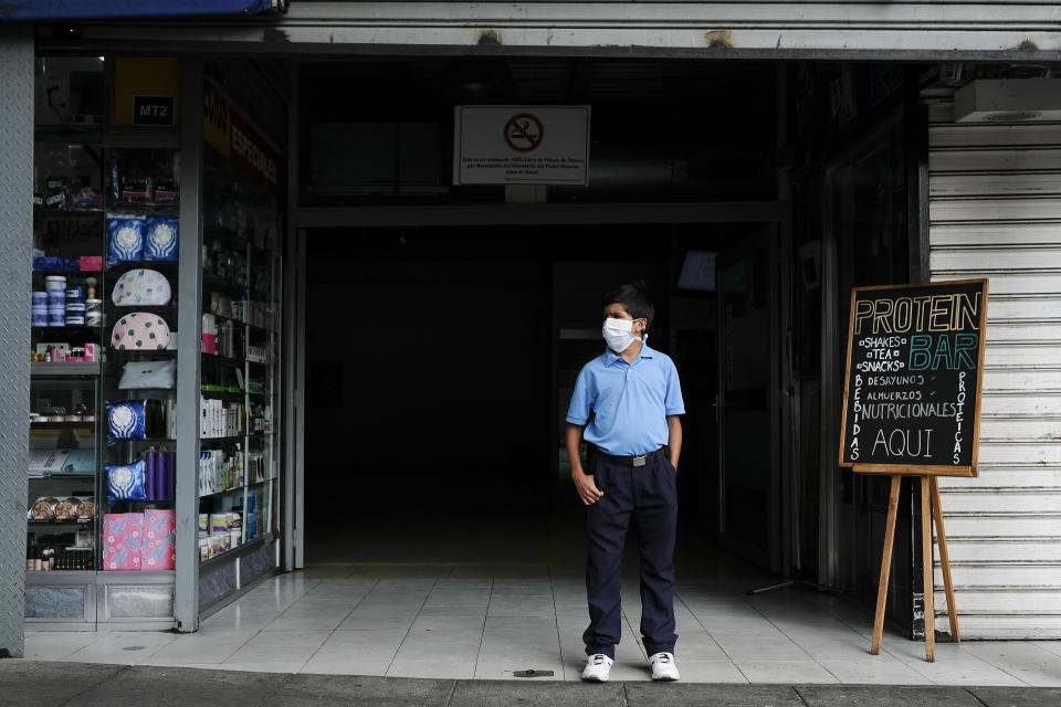A boy, wearing a protective mask as a precaution against the spread of the new coronavirus, stands outside a store waiting his mother to finish shopping, in Caracas, Venezuela, Friday, March 13, 2020. Venezuela's Vice President Delcy Rodriguez confirmed Friday the first two cases of the new coronavirus in the South American country. The vast majority of people recover from the new virus. (AP Photo/Matias Delacroix)