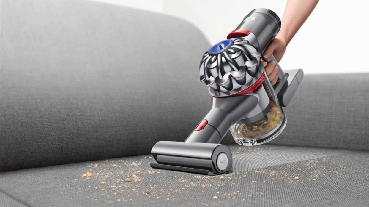  Dyson handheld vacuum cleaner cleaning up dirt from a sofa. 
