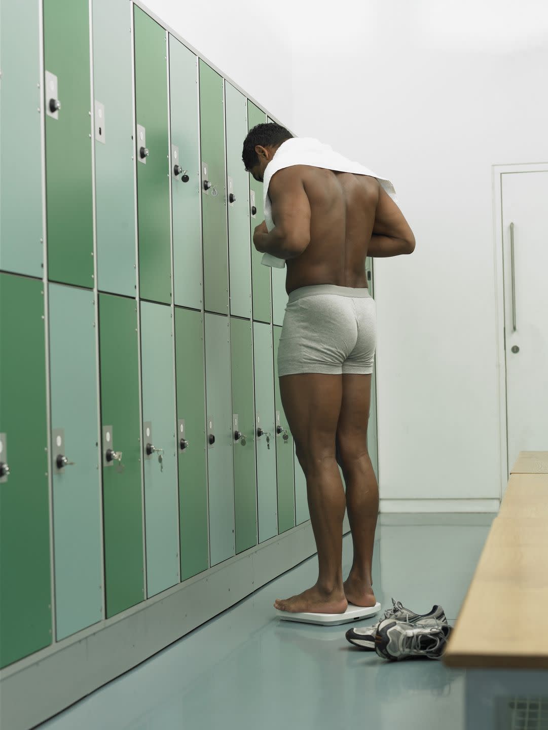 man standing on scales in locker room, rear view