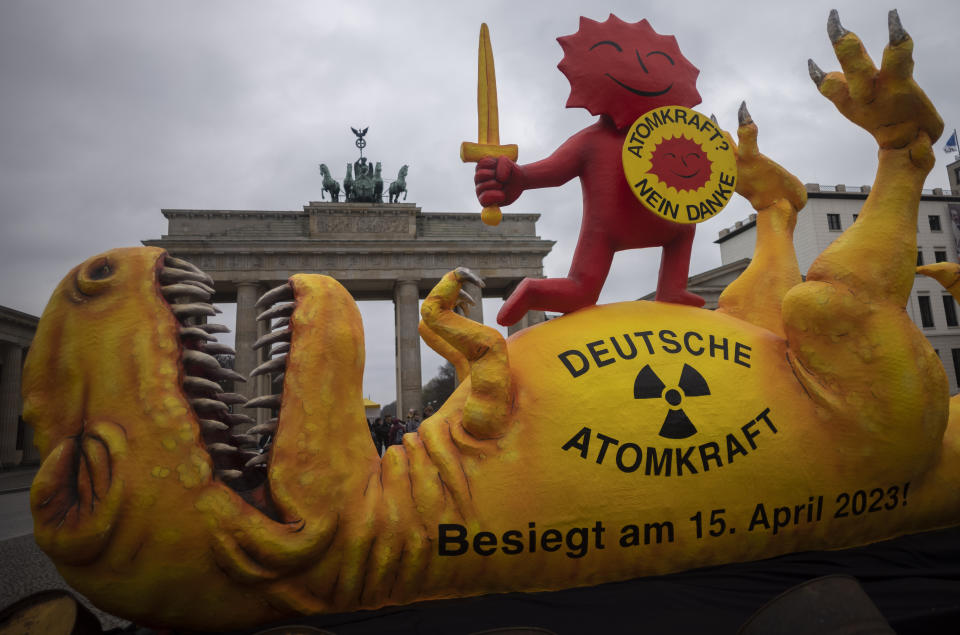 A mock-up dinosaur lies in front of the Brandenburg Gate during a rally marking the nuclear shutdown in Germany in Berlin, Germany, Saturday, April 15, 2023. Germany is shutting down its last three nuclear power plants on Saturday, April 15, 2023, as part of an energy transition agreed by successive governments. The signs read: 'Nuclear Power No Thanks' and the words on the dinosaur: 'German nuclear power defeated on April 15, 2023'. (AP Photo/Markus Schreiber)