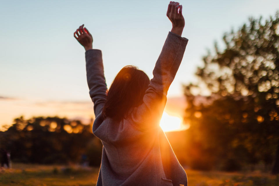 Someone stretches their arms against sunset in the sky