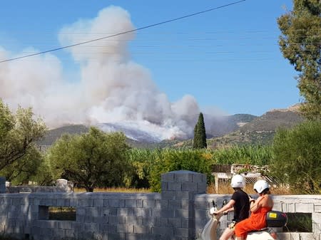 People look at the smoke rising from the side of a hill due to a wildfire on the island of Zakynthos