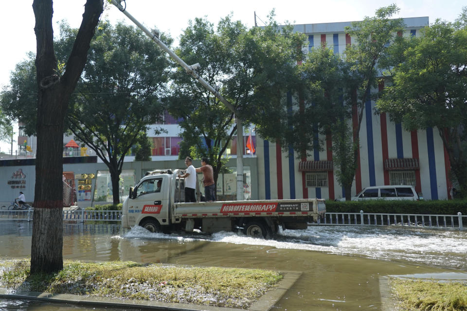 Men ride through flood waters in Xinxiang in central China's Henan province on Sunday, July 25, 2021. Trucks carrying water and food on Sunday streamed into the Chinese city at the center of flooding that killed dozens of people, while soldiers laid sandbags to fill gaps in river dikes that left neighborhoods under water. (AP Photo/Dake Kang)