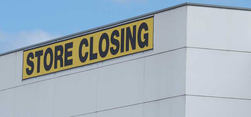 A yellow store closing banner at the top of a building.