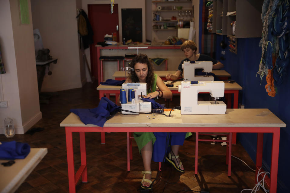 Textile artist Brooke Dennis, left, who is originally from New Zealand, makes scrubs for NHS (National Health Service) staff to wear during the coronavirus outbreak, at her textiles and craft studio called Make Town, in east London, Thursday, April 23, 2020, as part of the Scrub Hub network of voluntary community groups. The Scrub Hub just wanted to help, but they created a movement of volunteers responding to the coronavirus pandemic that has so far churned out more than 3,800 sets of scrubs for healthcare workers. (AP Photo/Matt Dunham)