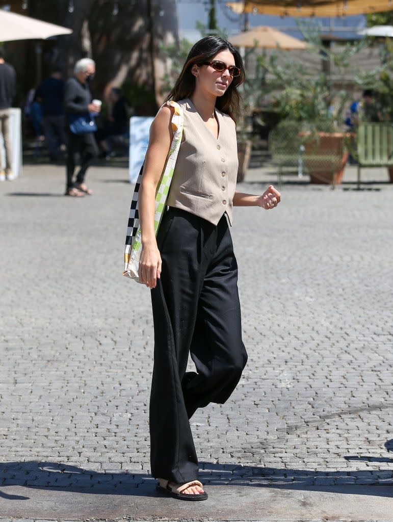 <p>While out in Los Angeles Kendall Jenner gave us all a masterclass in summer suiting. </p><p>The model and business owner paired an oat-hued waistcoat with black, high-waisted, wide-legged suit trousers to create a minimal workwear look. To give it a season-appropriate twist, the tequila brand owner added camel and black sandals, tortoiseshell 1990s-style sunnies and a bright <a href="https://int.stinegoya.com/products/idunn-bag-accessories-checks?switch=FR" rel="nofollow noopener" target="_blank" data-ylk="slk:checkerboard print bag by Stine Goya;elm:context_link;itc:0;sec:content-canvas" class="link ">checkerboard print bag by Stine Goya</a>.</p><p><a class="link " href="https://www.mytheresa.com/en-gb/frankie-shop-button-down-vest-1676098.html" rel="nofollow noopener" target="_blank" data-ylk="slk:SHOP WAISTCOAT NOW;elm:context_link;itc:0;sec:content-canvas">SHOP WAISTCOAT NOW</a></p>