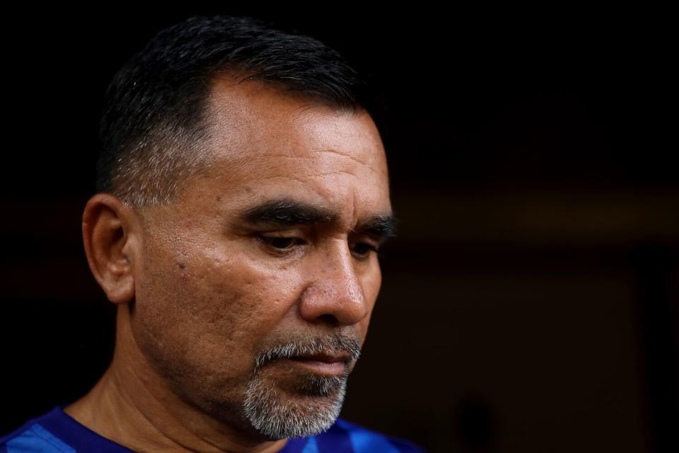 A man with dark, close-cropped hair and a salt-and-pepper beard, looking down