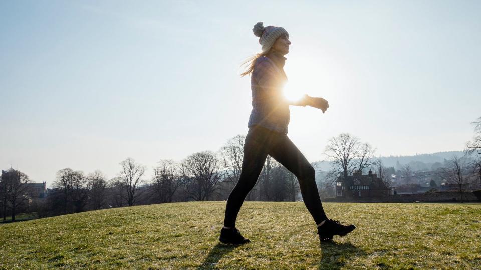 Woman walking across grass hill early in the morning wearing hat and gloves