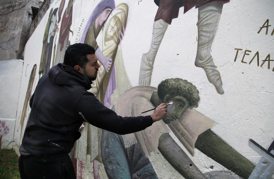 In this photo taken on Friday Feb. 21, 2014, Greek street artist Fikos paints a wall in the Kolonos area of Athens. The 27-year-old painter studied Byzantine art, influencing his work.(AP Photo/Dimitri Messinis)