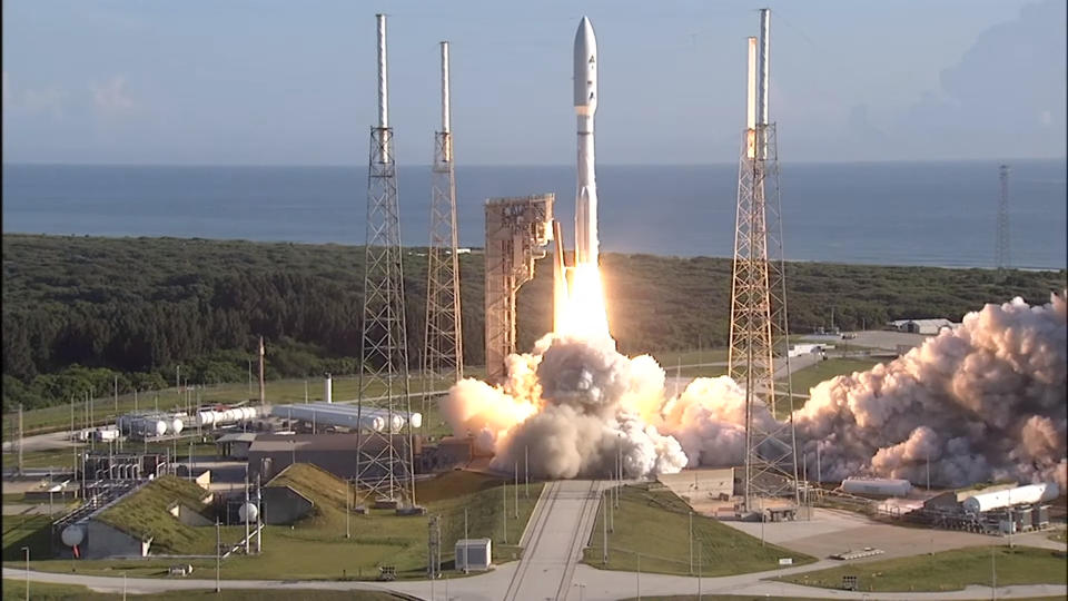 A white rocket with side boosters lifts off from a seaside launch pad