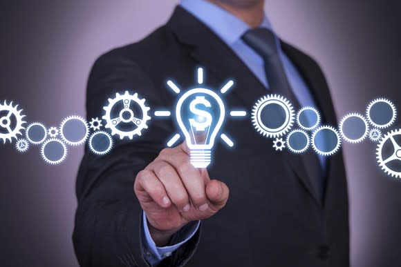 A businessman touching a screen showing a graphic of gears connected to a light bulb.