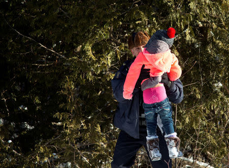 Royal Canadian Mounted Police (RCMP) officers assist a child from a family that claimed to be from Sudan as they walk across the U.S.-Canada border into Hemmingford, from into Hemmingford, Canada, from Champlain in New York, U.S., February 17, 2017. REUTERS/Christinne Muschi