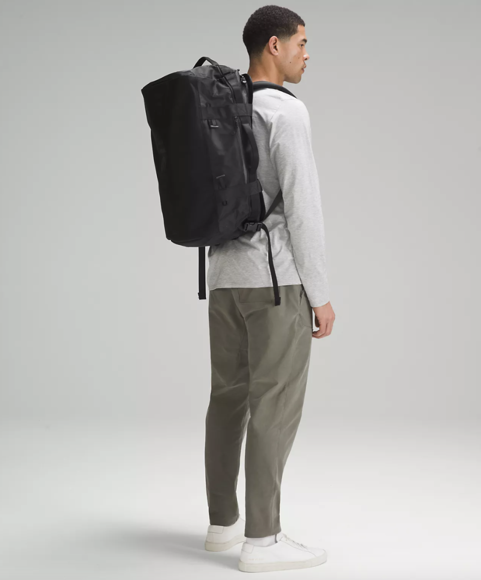 man wearing green pants, long sleeve t-shirt and black 2-in-1 Travel Duffle Backpack 45L (photo via lululemon)