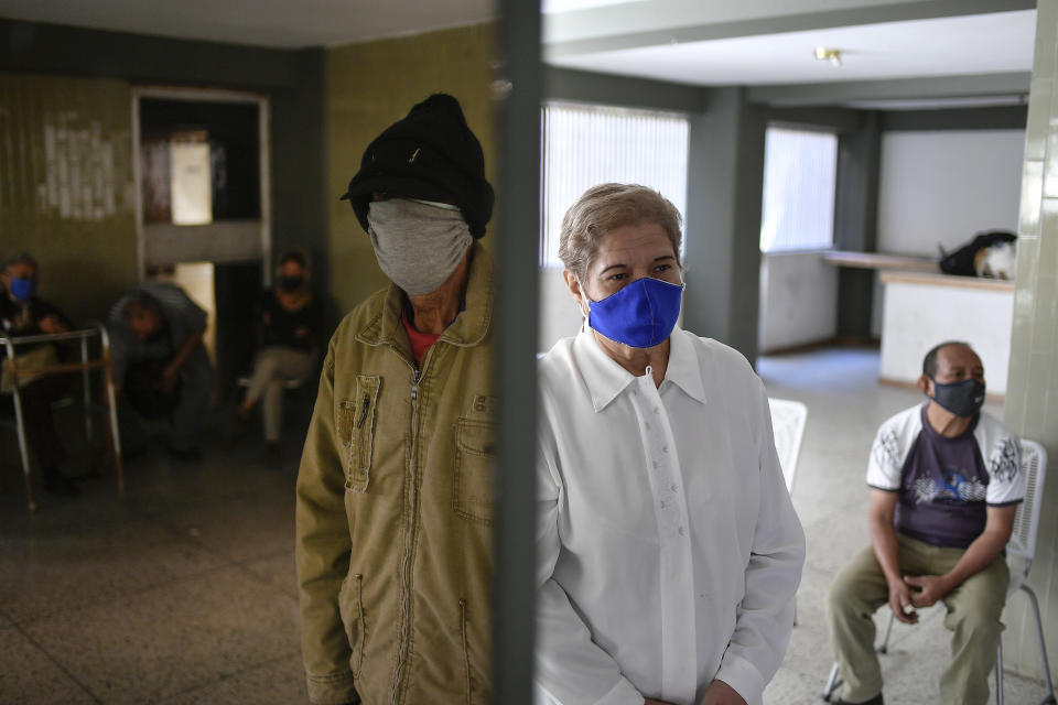 FILE - In this Jan. 14, 2021 file photo, residents, some reflected in a mirror, left, stand in their building's common area as they wait to get free, rapid COVID-19 tests during a volunteer testing campaign amid the new coronavirus pandemic, in the El Paraiso neighborhood of Caracas, Venezuela. The government of President Nicolás Maduro and the U.S.-backed opposition are accusing each other of playing politics with proposals to finance United Nations-supplied vaccines. (AP Photo/Matias Delacroix, File)