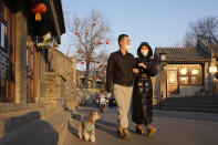 Residents wearing masks walk their dog along an alley way in Beijing, China, Tuesday, Jan. 11, 2022. The Chinese capital is on high alert ahead of the Winter Olympics as China locks down a third city elsewhere for COVID-19 outbreak. (AP Photo/Ng Han Guan)