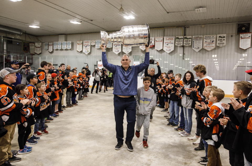 St. Louis Blues head coach Craig Berube, followed by his son Jake Berube, carries the Stanley Cup during a visit to his home town in Calahoo, Alberta, Tuesday July 2, 2019. (Jason Franson/The Canadian Press via AP)