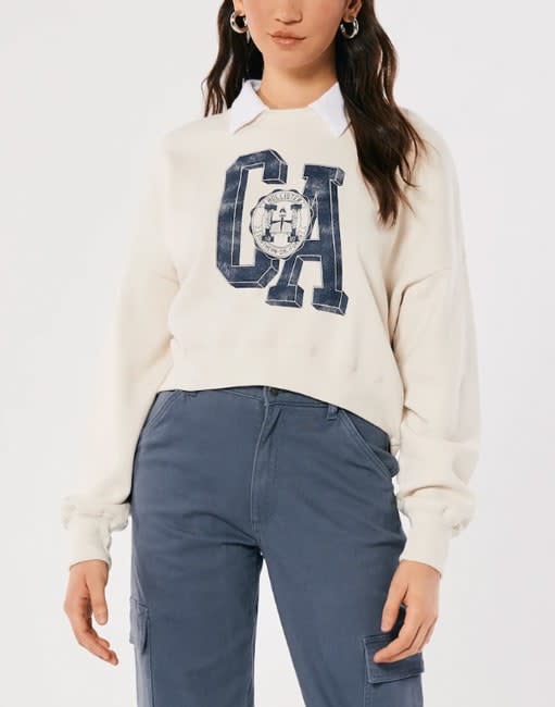 a mid shot of a model wearing a cream cropper sweater featuring the letters CA